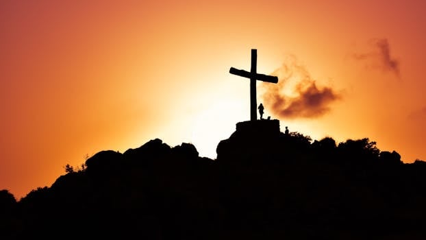 Majestic silhouette of a cross on a hill during a vivid sunset, symbolizing spirituality.